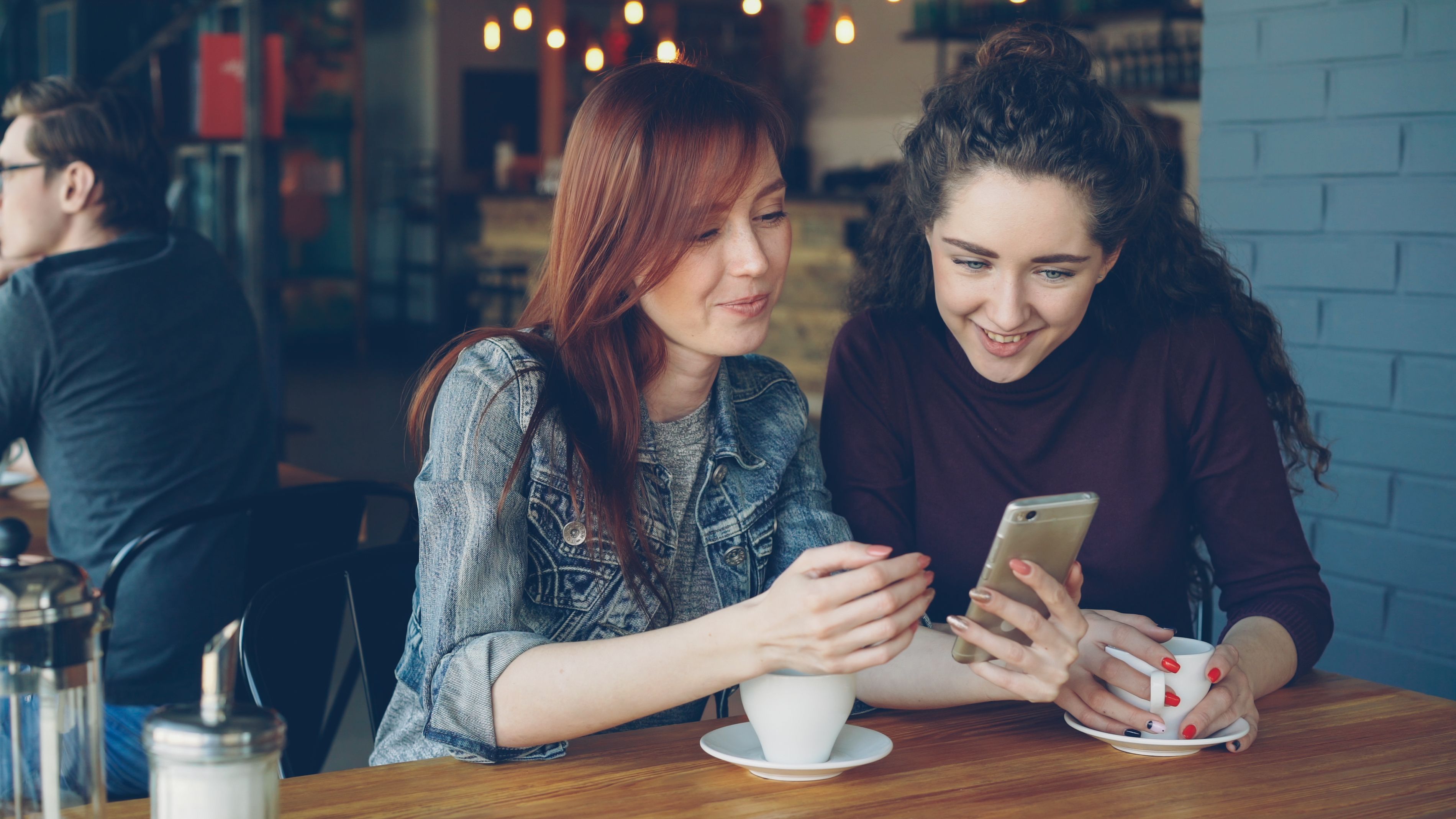 Two women sharing a conversation and looking at a phone over coffee