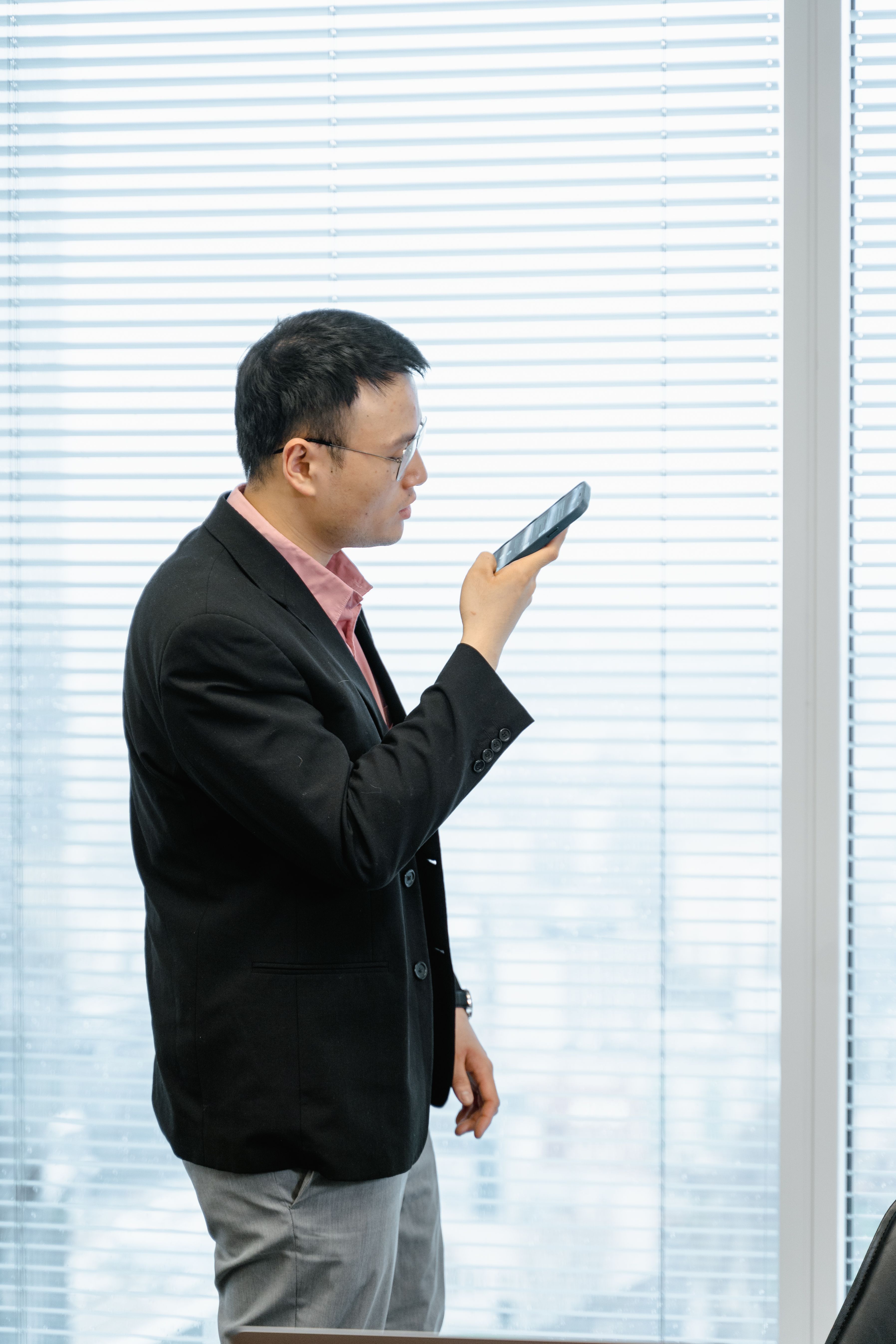 A man speaking a thought into his phone beside a bright window
